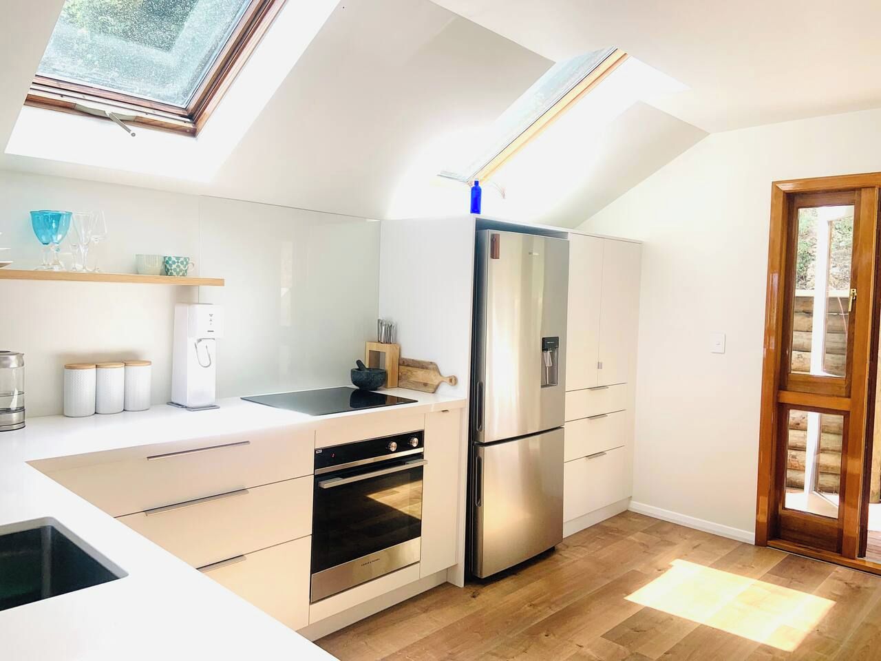 A modern kitchen with a built-in oven, a stainless steel refrigerator, and a skylight.