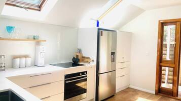 A modern kitchen with a built-in oven, a stainless steel refrigerator, and a skylight.