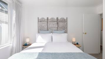 A bedroom with a large bed, two bedside tables, a headboard with intricate carvings, and a window with curtains.