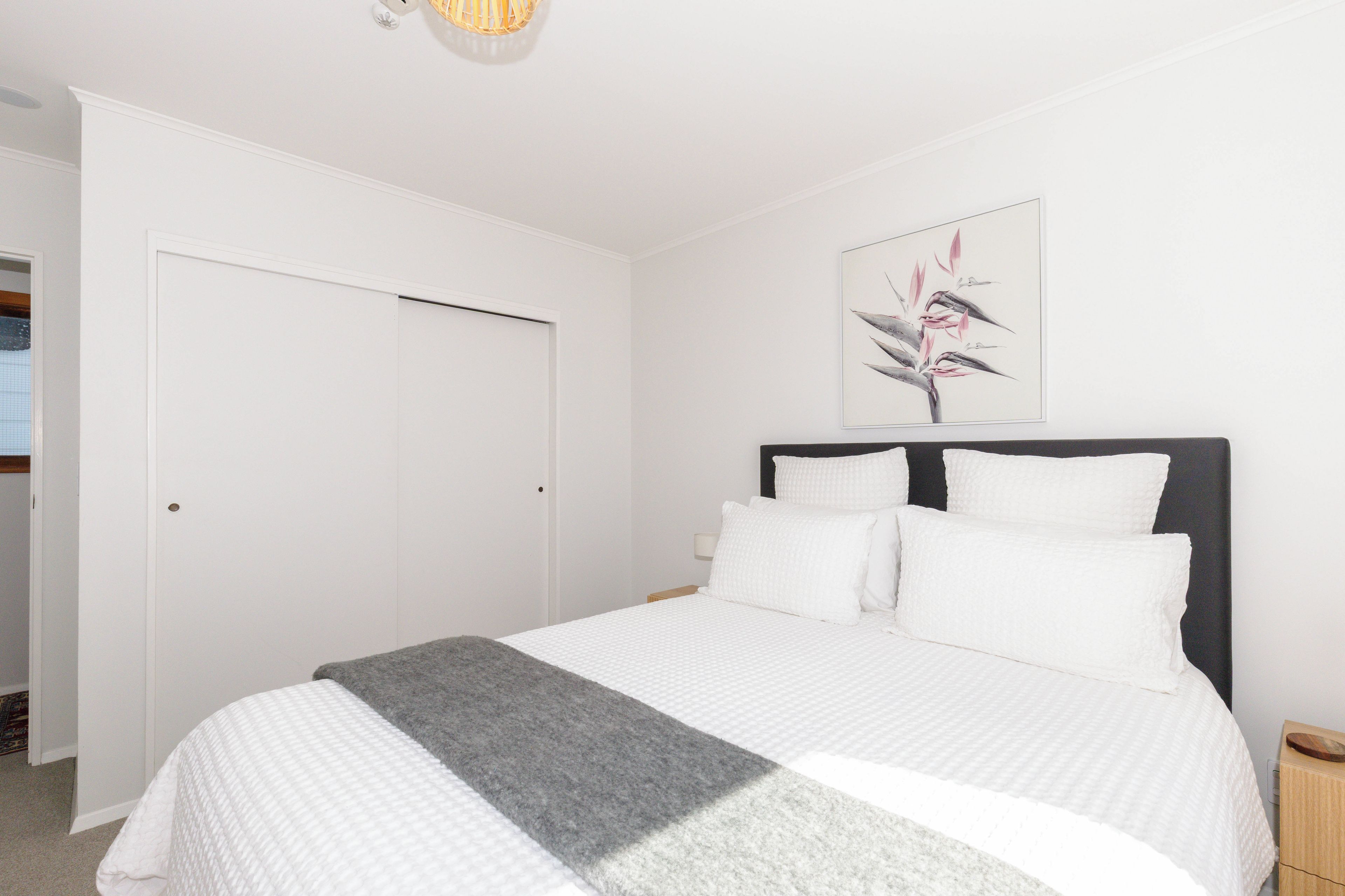Una camera da letto con un letto, pareti bianche, una porta e un quadro appeso al muro.