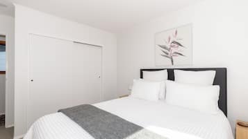 Une chambre à coucher avec un lit, des murs blancs, une porte et un tableau encadré accroché au mur.