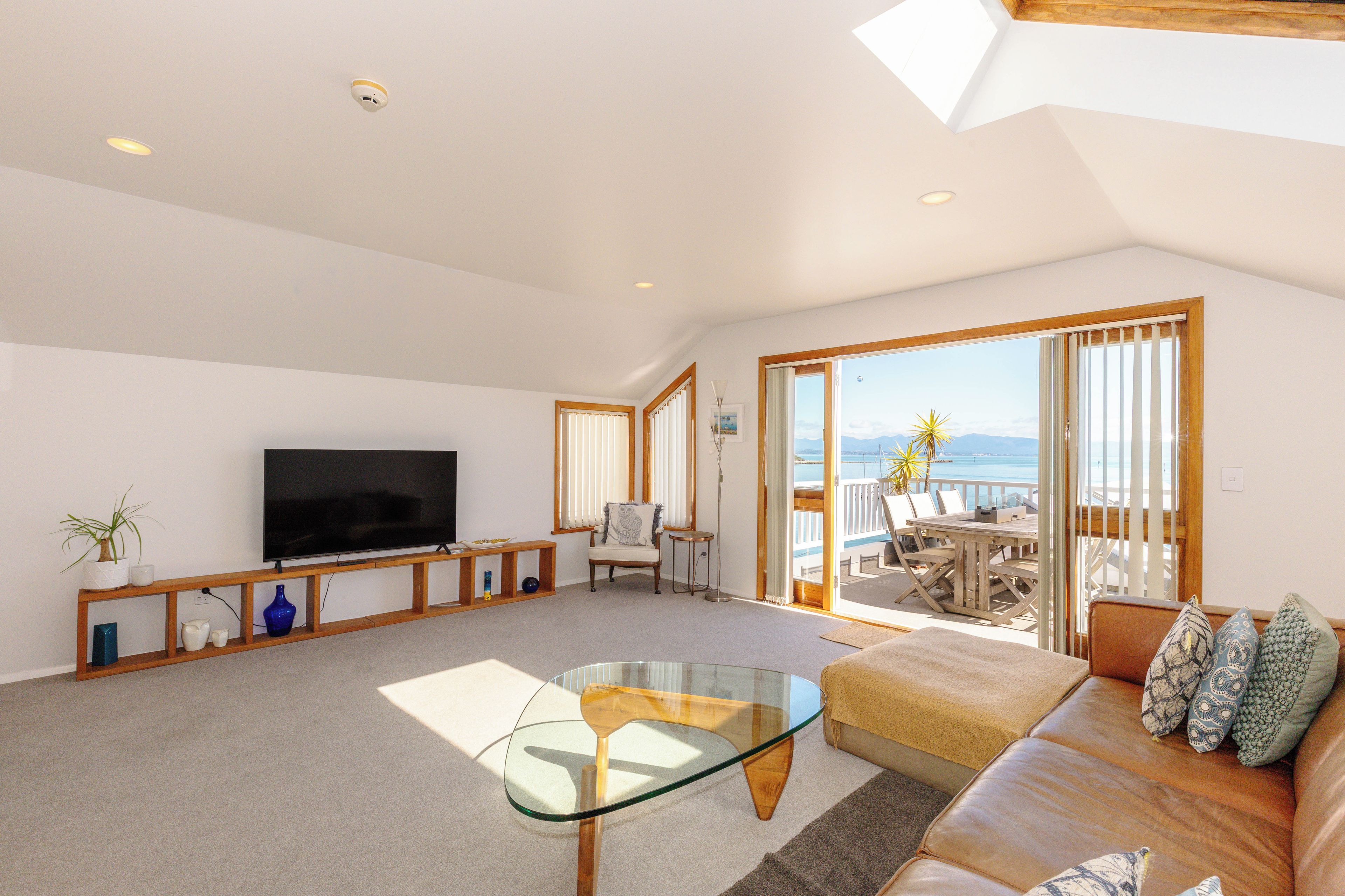 A spacious living room with a television, a glass coffee table, a sofa, and a view of the sea through large windows.