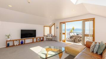 A spacious living room with a television, a glass coffee table, a sofa, and a view of the sea through large windows.