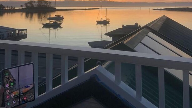 A balcony with a view of calm water and boats, a railing, and a person holding a smartphone. - Nelson Waterfront | Stunning Harbour Views | 2BR (Nelson)