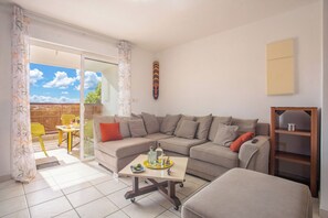 A living room with a sofa, a coffee table, a sliding glass door leading to an outdoor area with a table and chairs. - Le Cocon de Jojo - Balcon -Climatisation (LE ROBERT)
