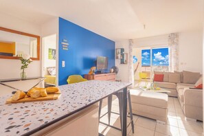 A modern living space with a kitchen area, a dining table, and a seating area with a sofa and chairs. - Le Cocon de Jojo - Balcon -Climatisation (LE ROBERT)