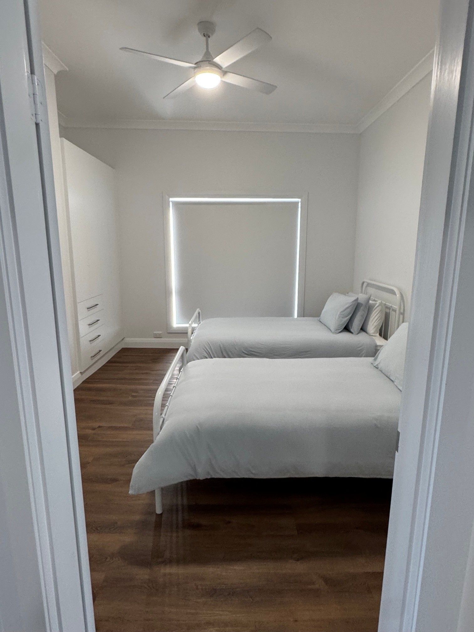 A bedroom with a bed, a ceiling fan, a window, and a wooden floor.