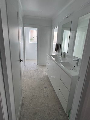 Une salle de bain avec un grand miroir, un lavabo et une porte donnant sur une autre pièce.