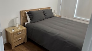 Ein Schlafzimmer mit einem Bett, einem Nachttisch aus Holz, einer Nachttischlampe und einem Fenster.