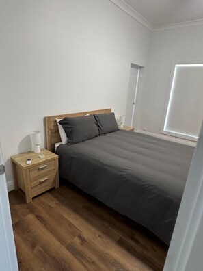 Une chambre à coucher avec un lit, une table de chevet en bois, une lampe de chevet et une fenêtre.