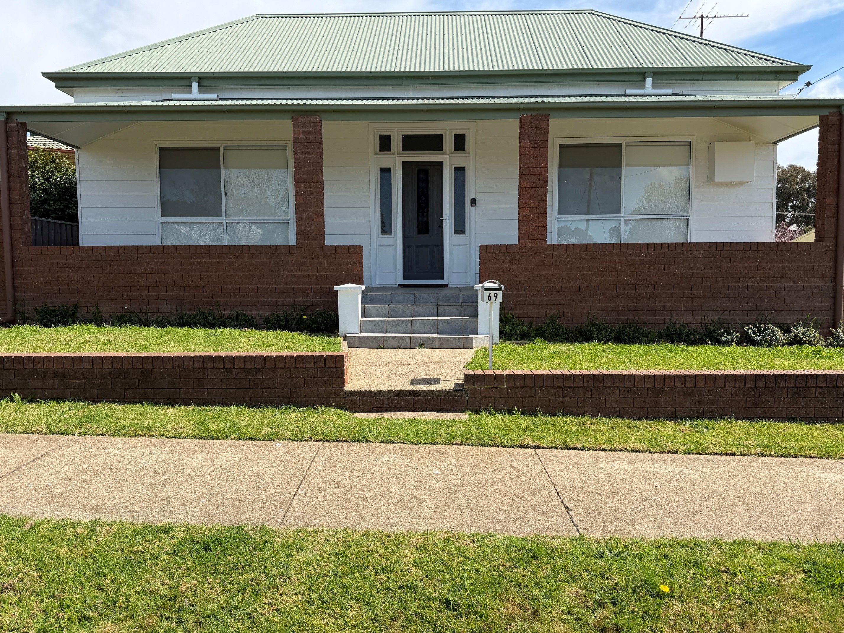 A single-story house with a front porch, a mailbox, and a number 69 sign.