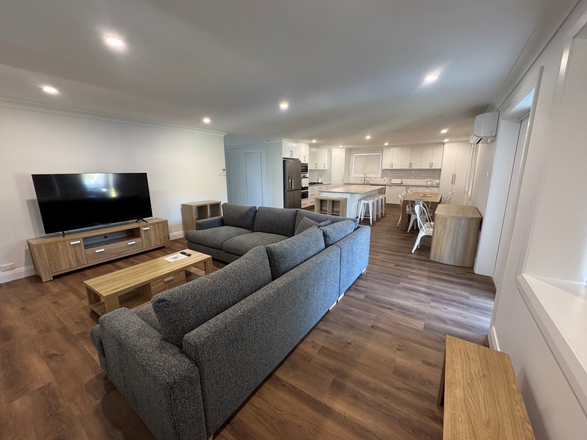A modern living room with a large sectional sofa, a flat-screen TV, and a wooden coffee table.
