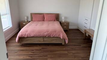 Quarto com cama de madeira, mesa de cabeceira, cômoda e ventilador de teto.