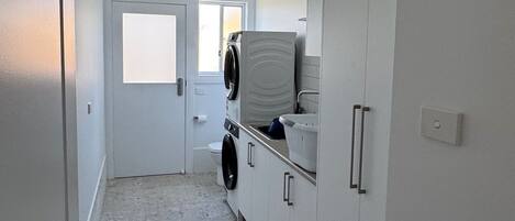 A narrow hallway with a washing machine and dryer, a door leading to another room, and a light switch on the wall.