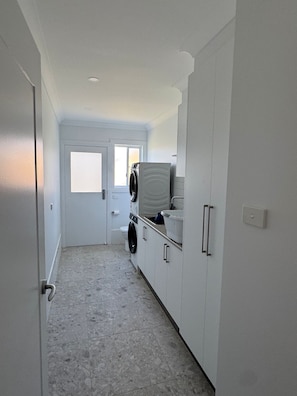 A narrow hallway with a washing machine and dryer, a door leading to another room, and a light switch on the wall.