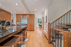 A modern kitchen with a central island, bar stools, wooden cabinets, and a stainless steel refrigerator. - Singing Pass at Fitzsimmons Walk (Whistler)