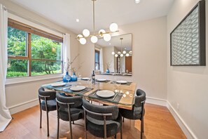 A dining area with a glass table, six chairs, a chandelier, and a large mirror. - Singing Pass at Fitzsimmons Walk (Whistler)