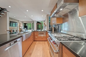 A modern kitchen with stainless steel appliances, wooden cabinets, and a built-in oven. - Singing Pass at Fitzsimmons Walk (Whistler)