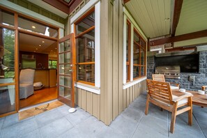 A patio area with a stone fireplace, wooden furniture, and a sliding glass door leading to an interior space. - Singing Pass at Fitzsimmons Walk (Whistler)
