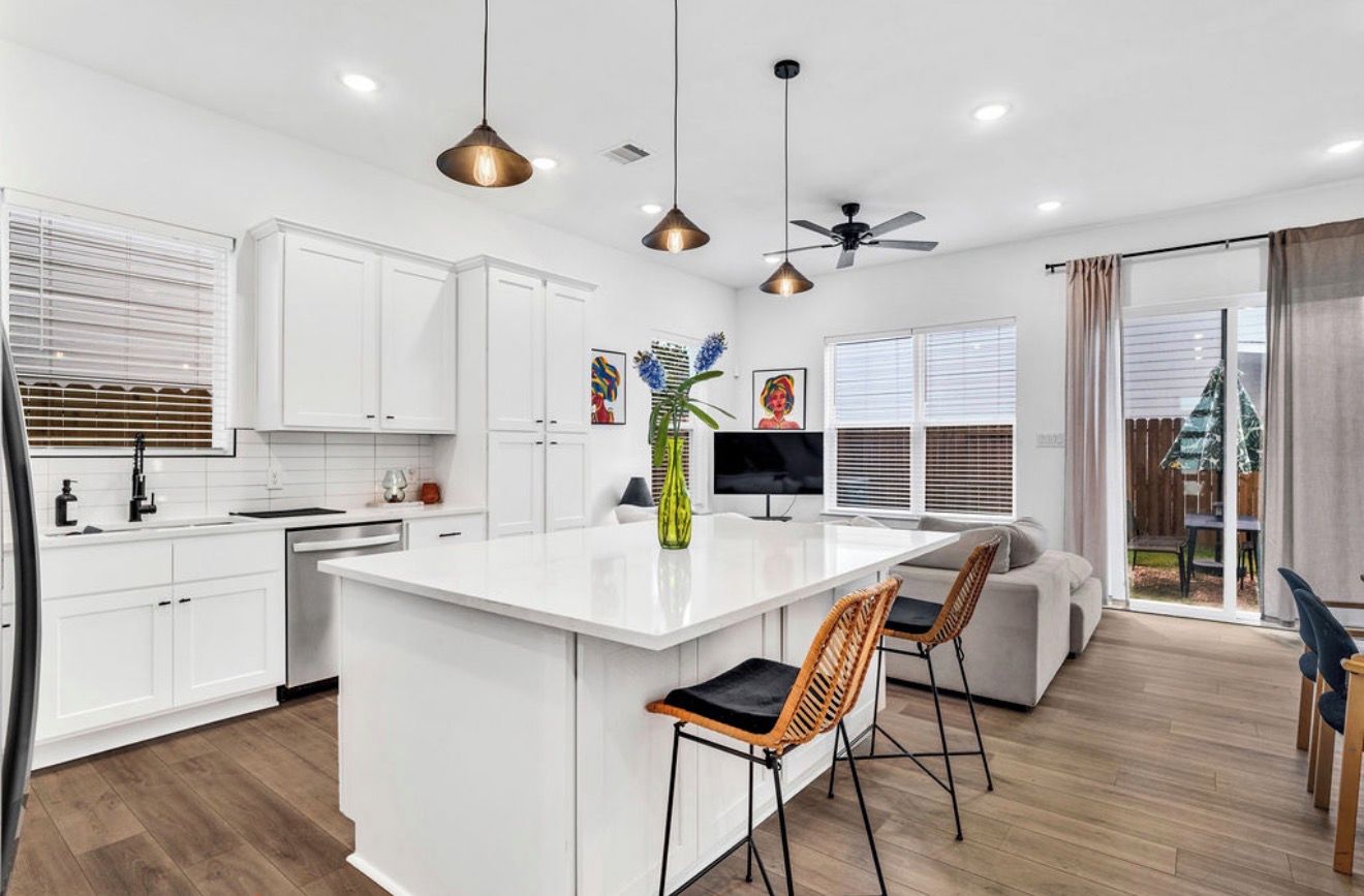 Una cocina moderna con armarios blancos, una isla central, iluminación colgante y un ventilador de techo.