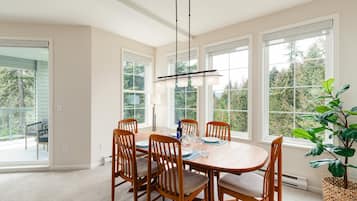 A dining area with a wooden table and chairs, large windows, and a hanging light fixture.