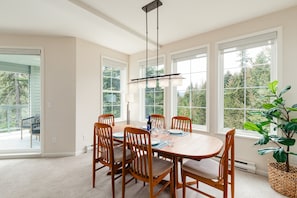 Un comedor con una mesa y sillas de madera, ventanas amplias y una lámpara colgante.