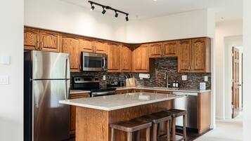 A modern kitchen with wooden cabinets, stainless steel appliances, a granite countertop, and a built-in island with bar stools.