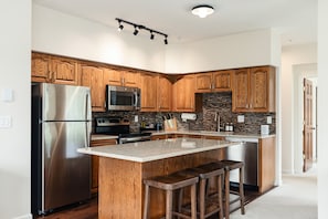 Una cocina moderna con armarios de madera, electrodomésticos de acero inoxidable, encimera de granito y una isla integrada con taburetes de bar.
