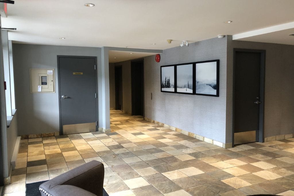 A hotel lobby with a checkered floor, a sofa, a wall-mounted picture, and a door with a sign.