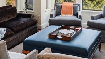 A living room with a dark brown sofa, two grey armchairs, a blue ottoman, and a wooden tray with books.