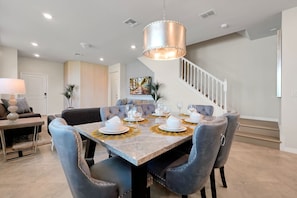 A dining area with a marble table, grey upholstered chairs, and a chandelier. - Dream Family Escape Pool and Themed Rooms (Clermont)