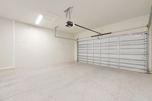 A clean, empty garage with a closed metal garage door, a ceiling-mounted projector, and a white brick wall. - Dream Family Escape Pool and Themed Rooms (Clermont)