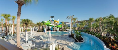 Zona de piscina en un resort con tobogán de agua, sillas de descanso y palmeras.