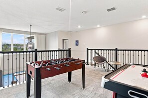 A room with a foosball table, a pool table, and a view of a residential area through large windows. - Perfect Family Escape Pool Themed Rooms (Kissimmee)
