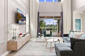 A spacious living room with a large flat-screen TV mounted on the wall, a comfortable grey sofa, a coffee table, and a sideboard with decorative items. - Perfect Family Escape Pool Themed Rooms (Kissimmee)