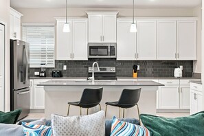 A modern kitchen with white cabinets, a central island, a refrigerator, a microwave, and a toaster. - Perfect Family Escape Pool Themed Rooms (Kissimmee)