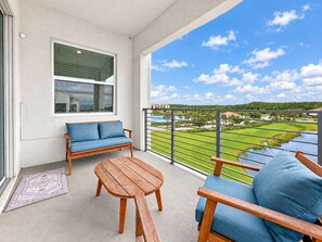 A balcony with a sofa, a table, and a view of a golf course. - Lake View Family Escape 2BR Close to Disney (Kissimmee)