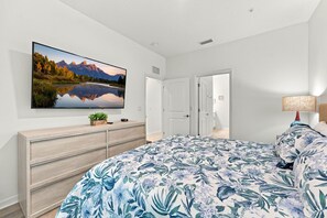 A bedroom with a bed, a dresser, a flat-screen TV on the wall, and a door. - Lake View Family Escape 2BR Close to Disney (Kissimmee)