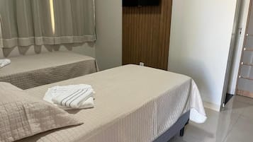 Habitación de hotel con dos camas, un televisor de pantalla plana montado en la pared y una puerta corredera que da a otra habitación.