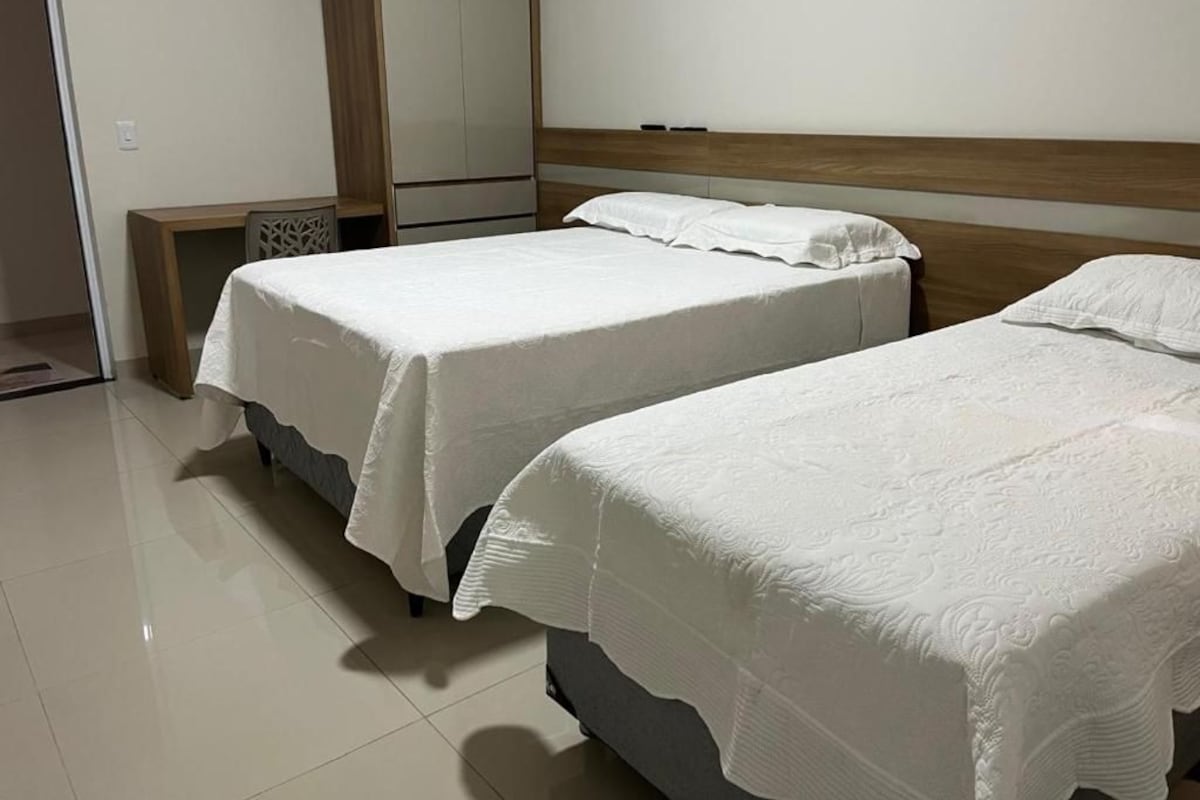Habitación de hotel con dos camas, un cabecero de madera y una mesita con una silla.