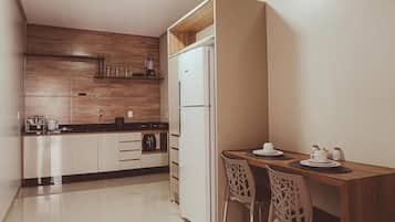 Cocina compacta con refrigerador, cafetera y comedor con mesa y sillas.