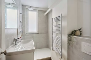 Une salle de bain moderne équipée d’un lavabo, d’un miroir, d’une douche et d’un porte-serviettes.