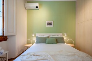 A bedroom with a bed, two bedside tables, an air conditioning unit, a framed picture on the wall, and a window with curtains. - Private garden and terrace · Convenient parking (FIRENZE)