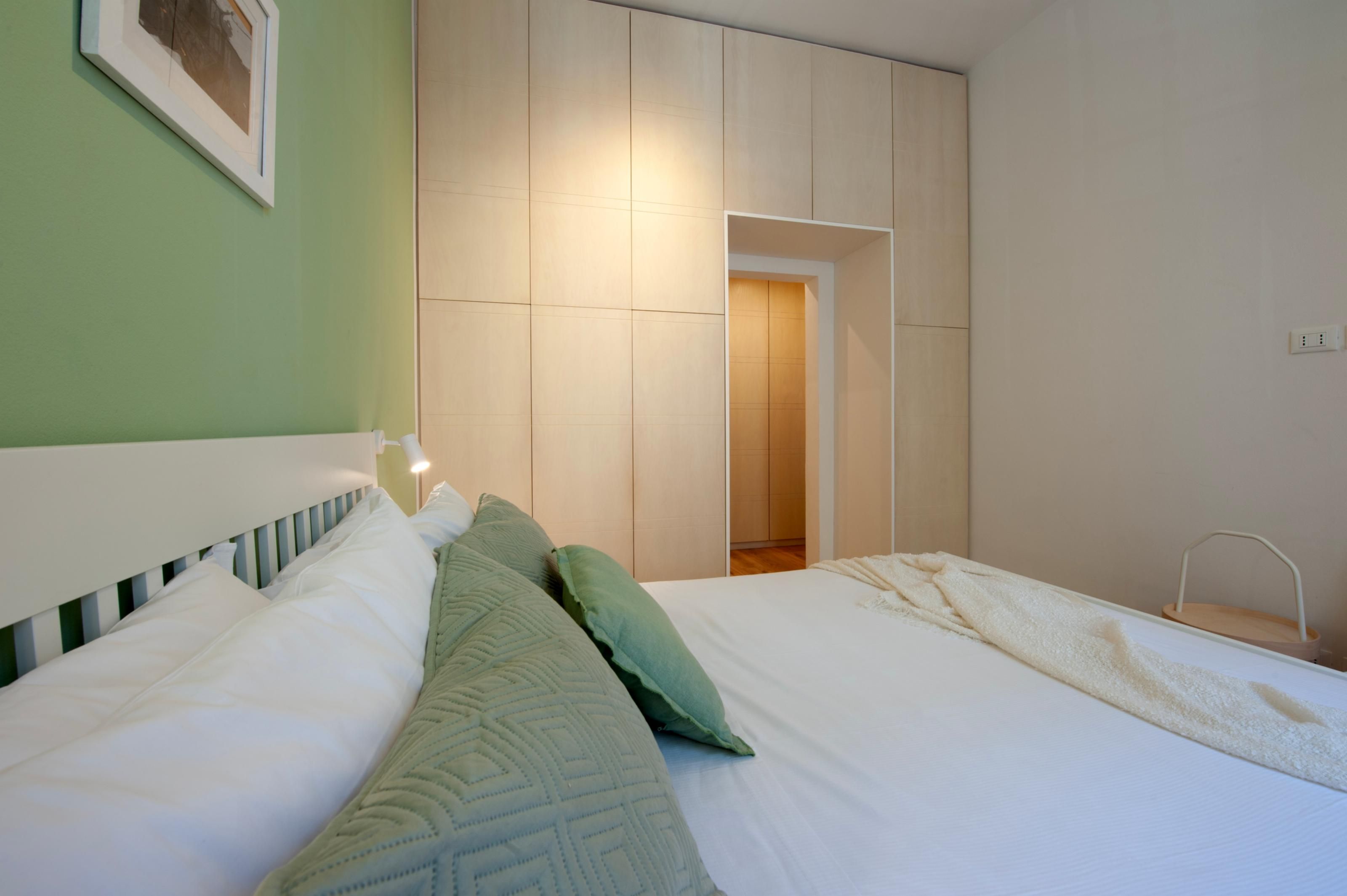 Ein Schlafzimmer mit einem Bett, Kissen, einer Nachttischlampe und einem Kleiderschrank.