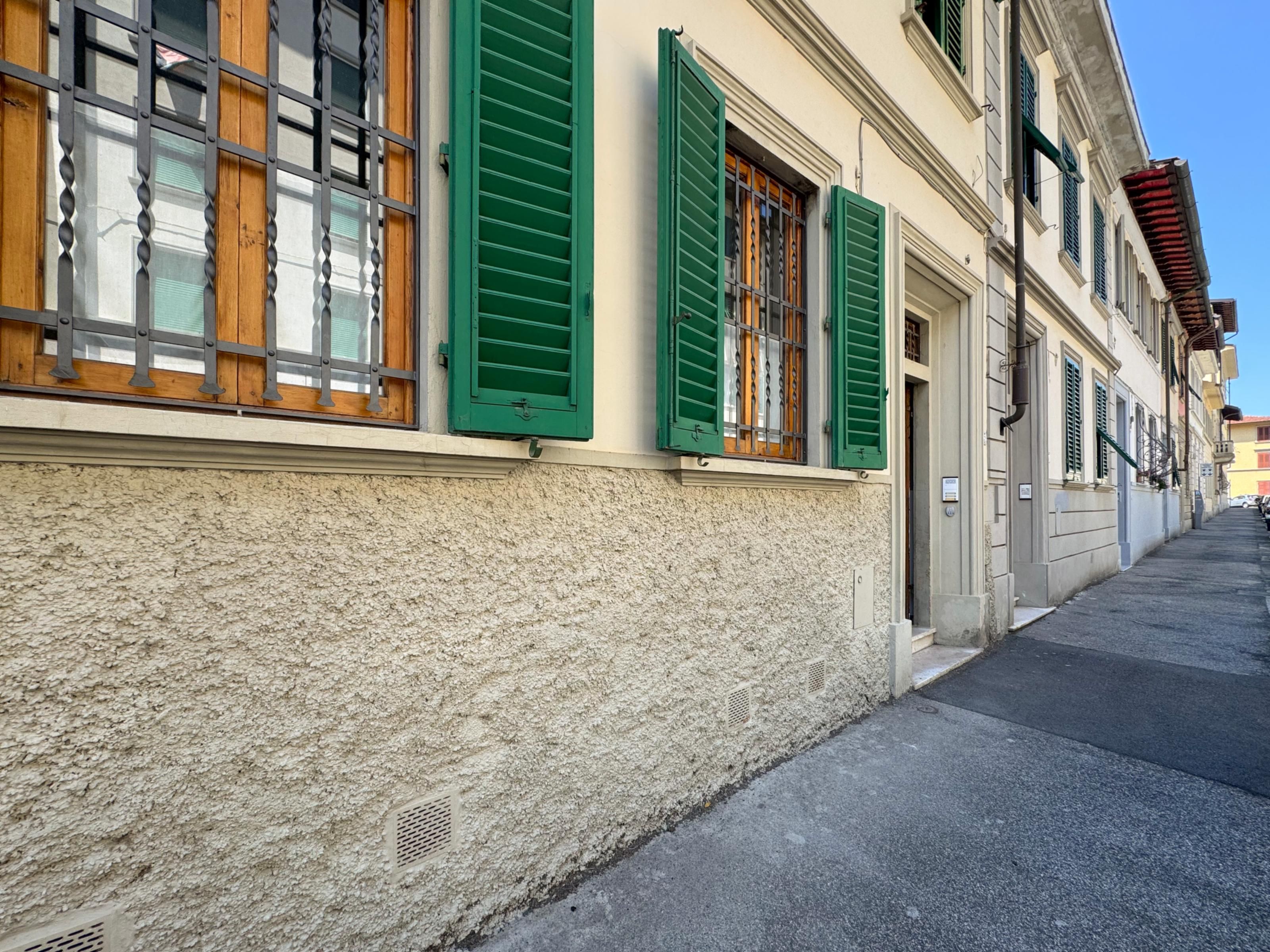 Ein Gebäude mit strukturierter Fassade, grünen Fensterläden und einer schmalen Straße.