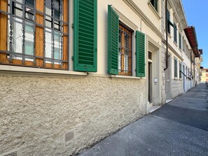 Ein Gebäude mit strukturierter Fassade, grünen Fensterläden und einer schmalen Straße.