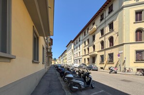 A street lined with parked motorcycles and cars, buildings with arched windows, and a clear blue sky. - Private garden and terrace · Convenient parking (FIRENZE)
