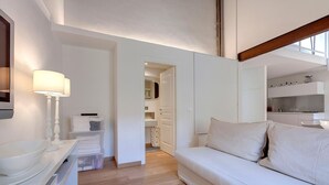 Ein modernes Interieur mit einem weißen Sofa, einem Nachttisch mit Lampe und Blick in eine Küchenzeile.