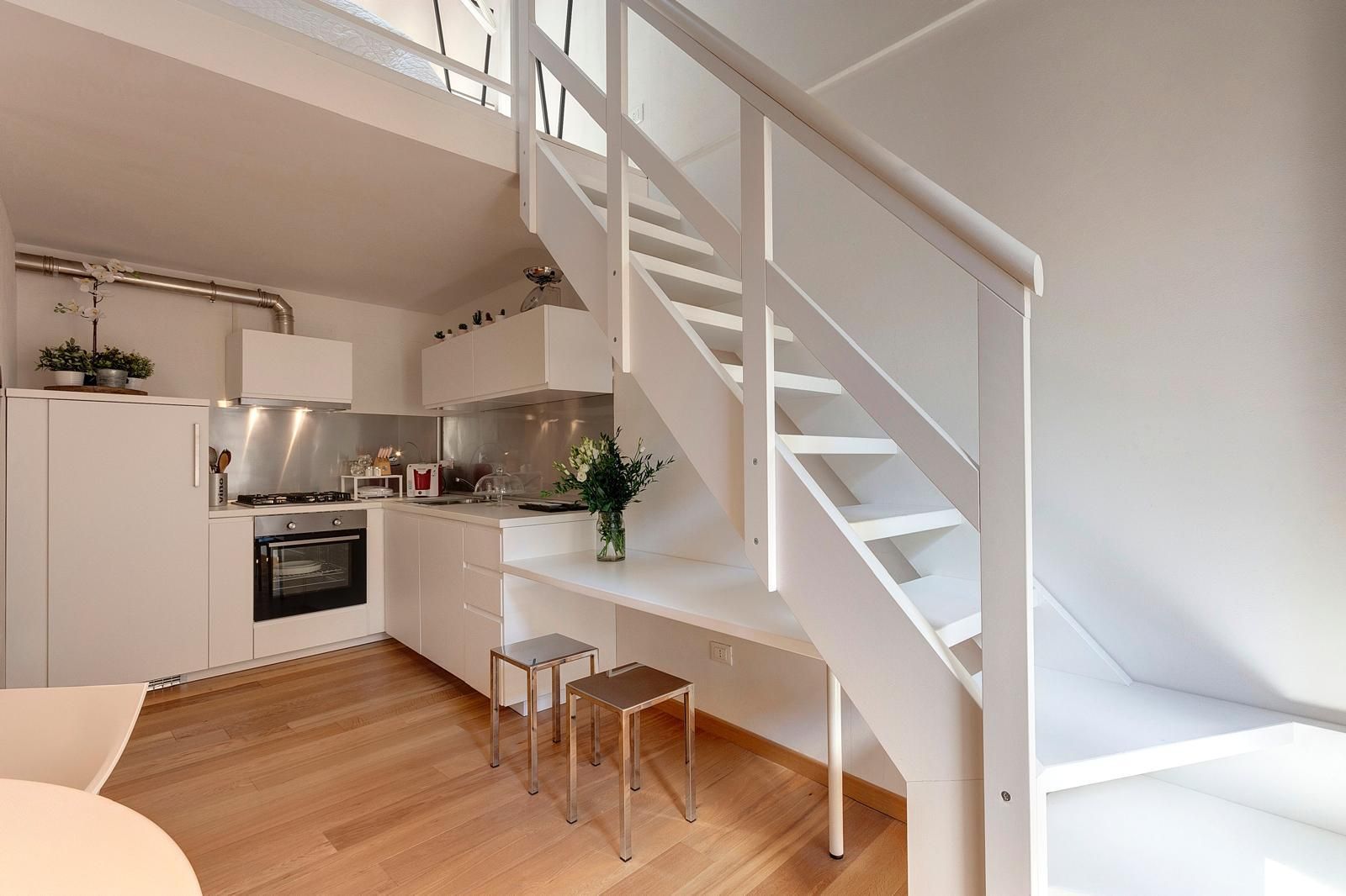 A modern kitchen with white cabinetry, a stainless steel stove, and a wooden floor.