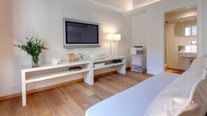 Ein modernes Hotelzimmer mit Flachbildfernseher, Nachttisch mit Lampen, einem großen Bett und einem begehbaren Kleiderschrank.